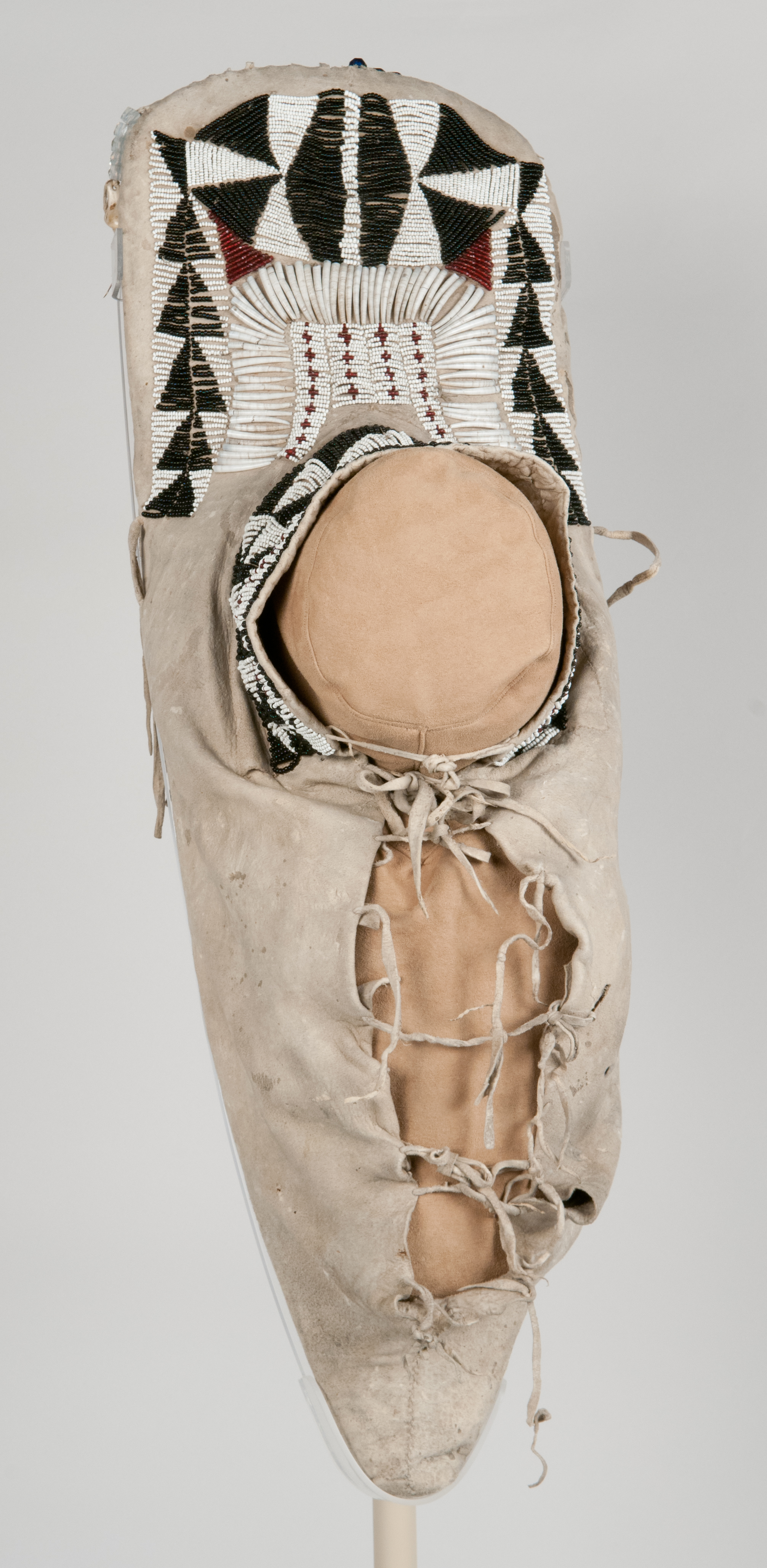 Teardrop shaped child's cradleboard made from a wooden board and covered with brain tanned deerskin. Decorated with  glass beads, dentalium shells, and elk teeth. 